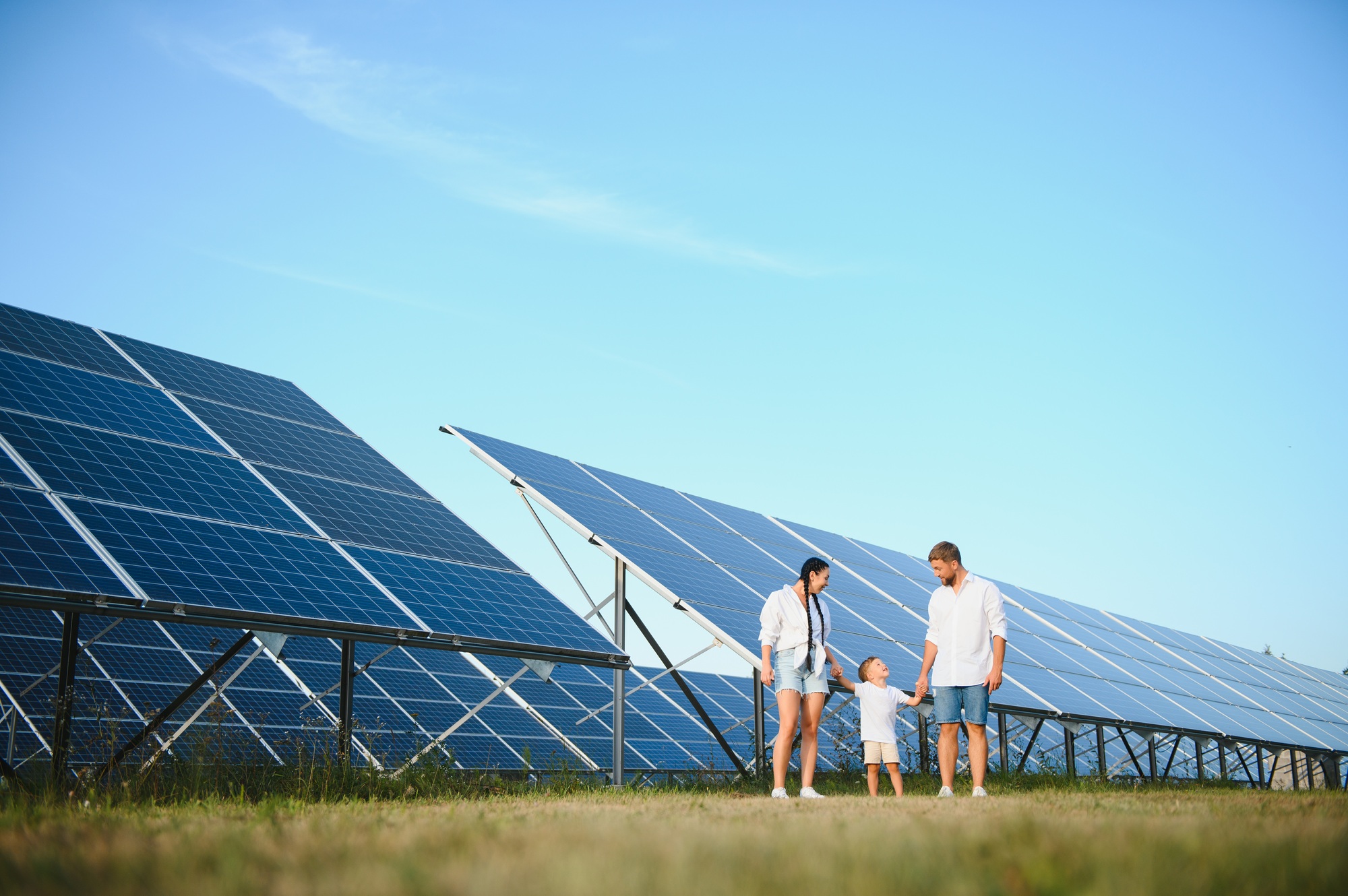 A wide shot of a happy family standing together and smiling at camera with a large solar panel