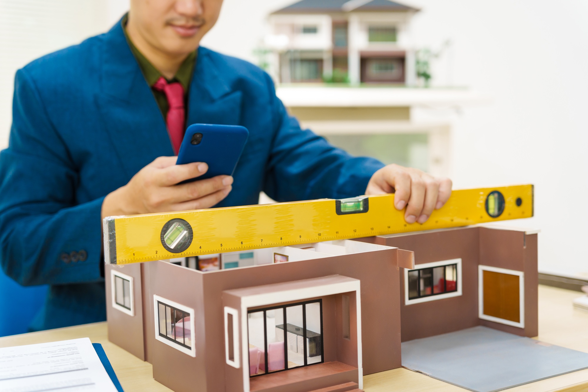 Asian architect in a suit works alone with laptop, paperwork, blueprints for mortgage project.